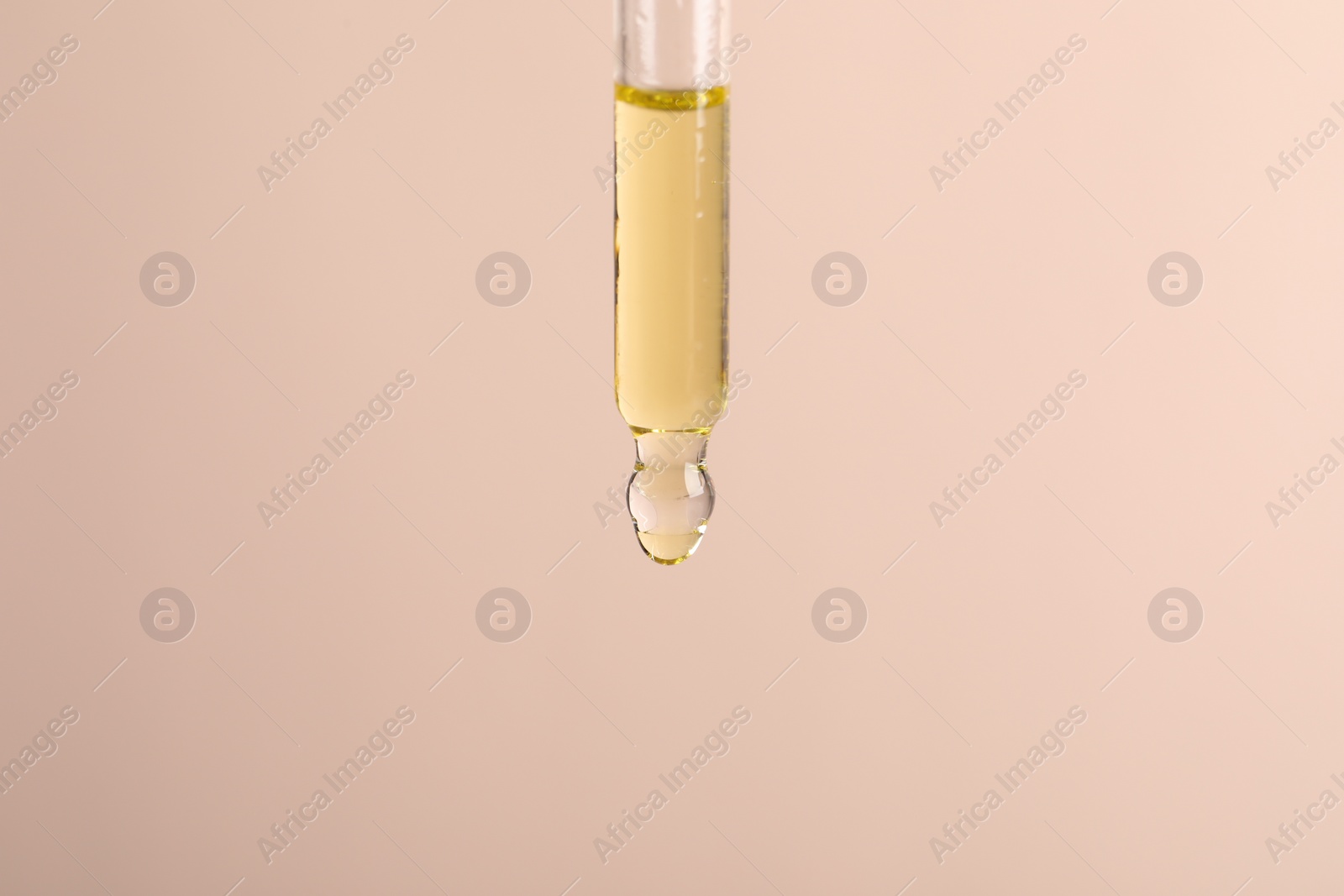 Photo of Dripping cosmetic serum from pipette on beige background