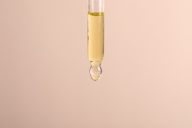 Dripping cosmetic serum from pipette on beige background