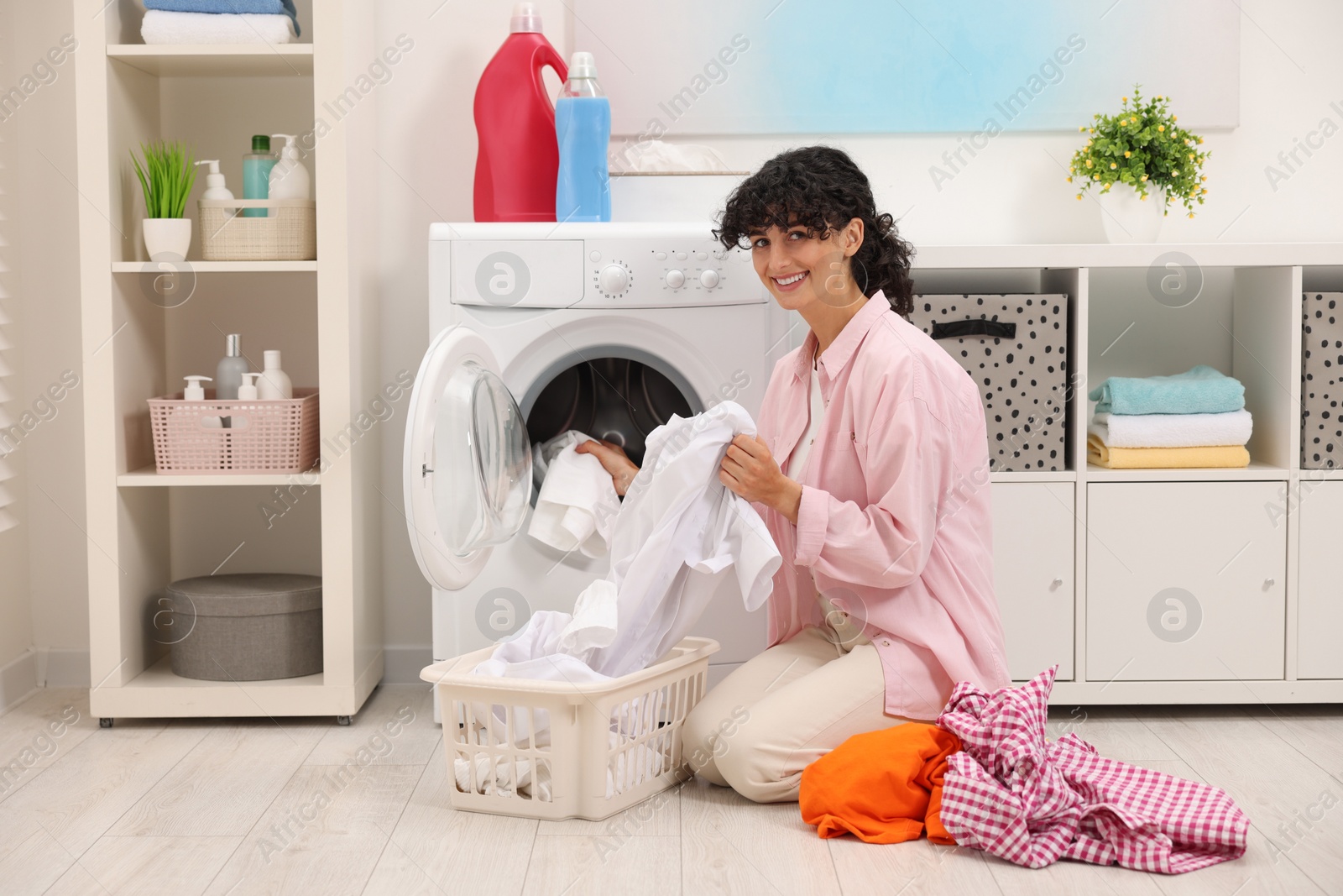 Photo of Happy woman putting laundry into washing machine indoors