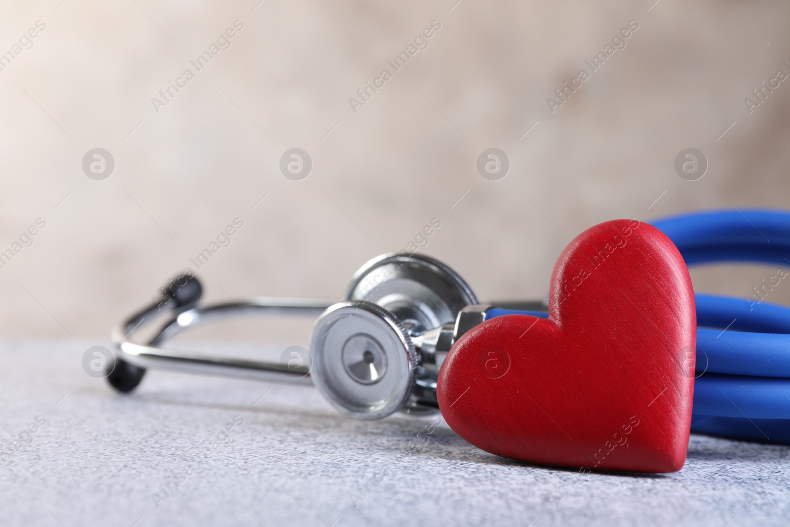 Photo of Stethoscope and red heart on grey stone table, closeup. Space for text