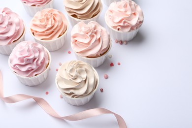 Many tasty cupcakes, sprinkles and ribbon on white background