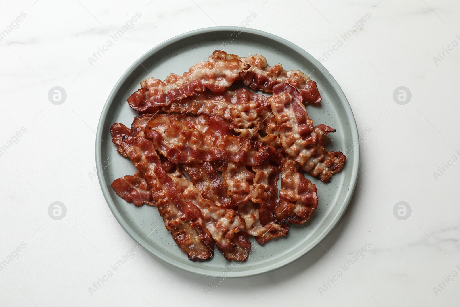 Photo of Slices of tasty fried bacon on white marble table, top view