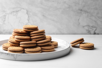 Tasty sandwich cookies with cream on white table