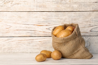 Photo of Sack with fresh organic potatoes and space for text on wooden background