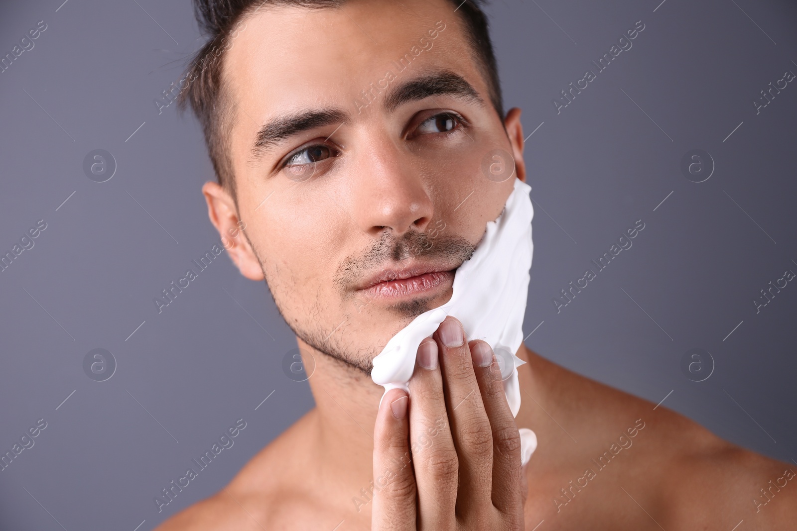 Photo of Handsome young man applying shaving foam on color background