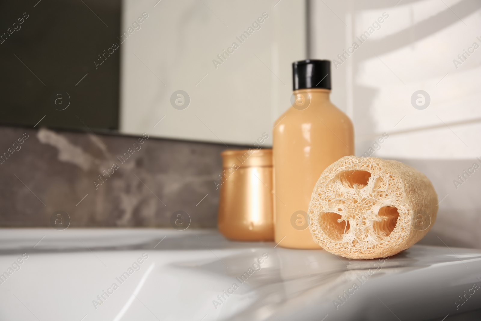 Photo of Natural loofah sponge and cosmetic products on washbasin in bathroom. Space for text