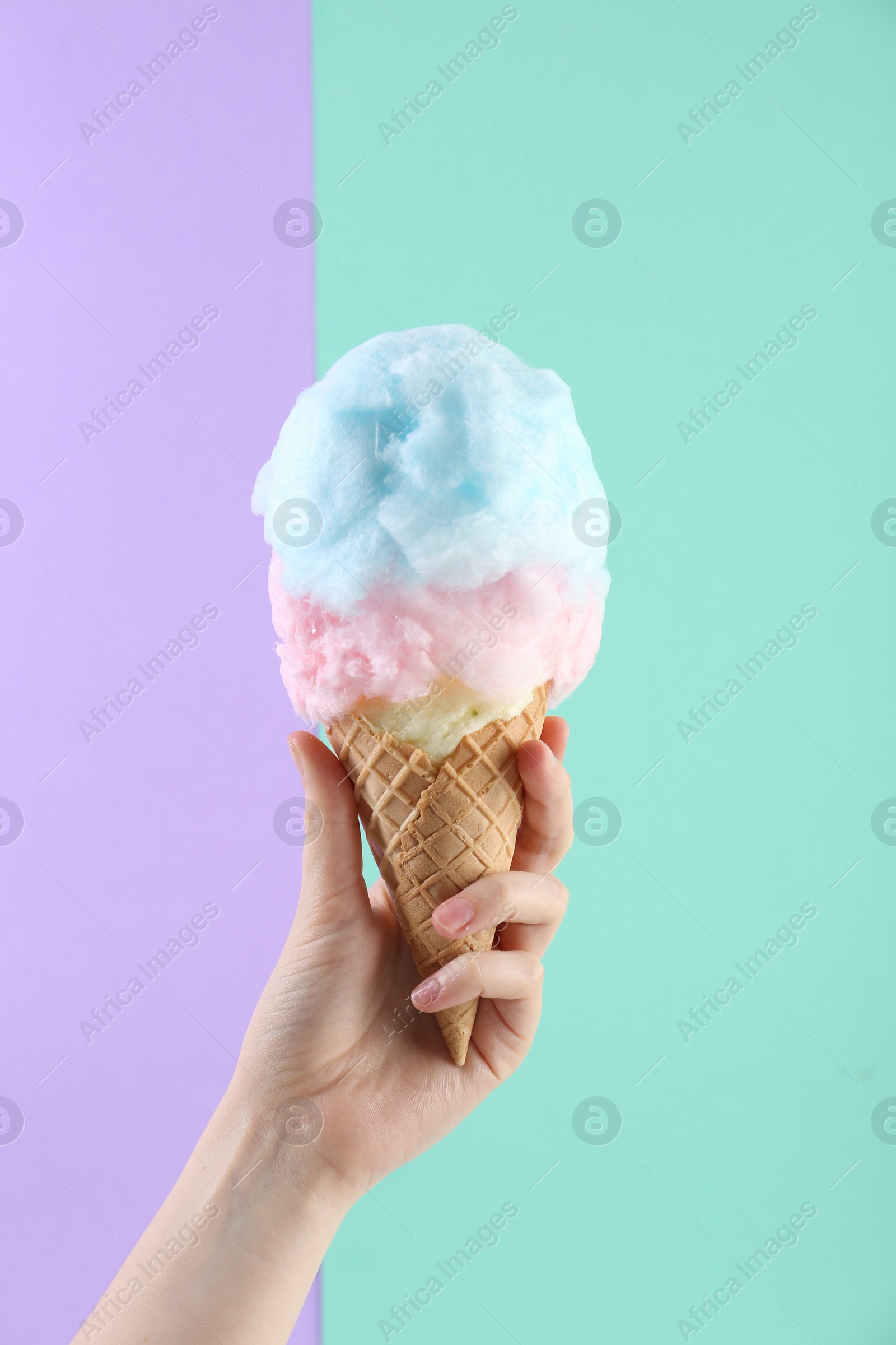 Photo of Woman holding waffle cone with cotton candy on color background, closeup