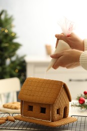 Woman making gingerbread house at table indoors, closeup