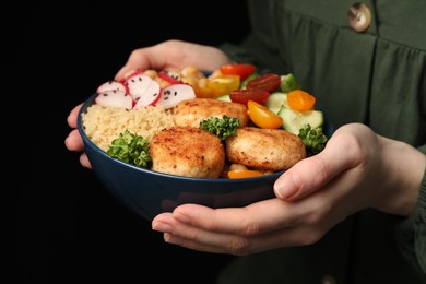Photo of Woman holding delicious vegan bowl with cutlets and cucumbers on black background, closeup