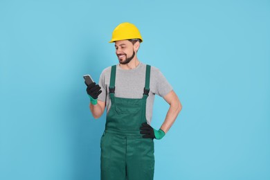 Professional repairman in uniform with phone on light blue background