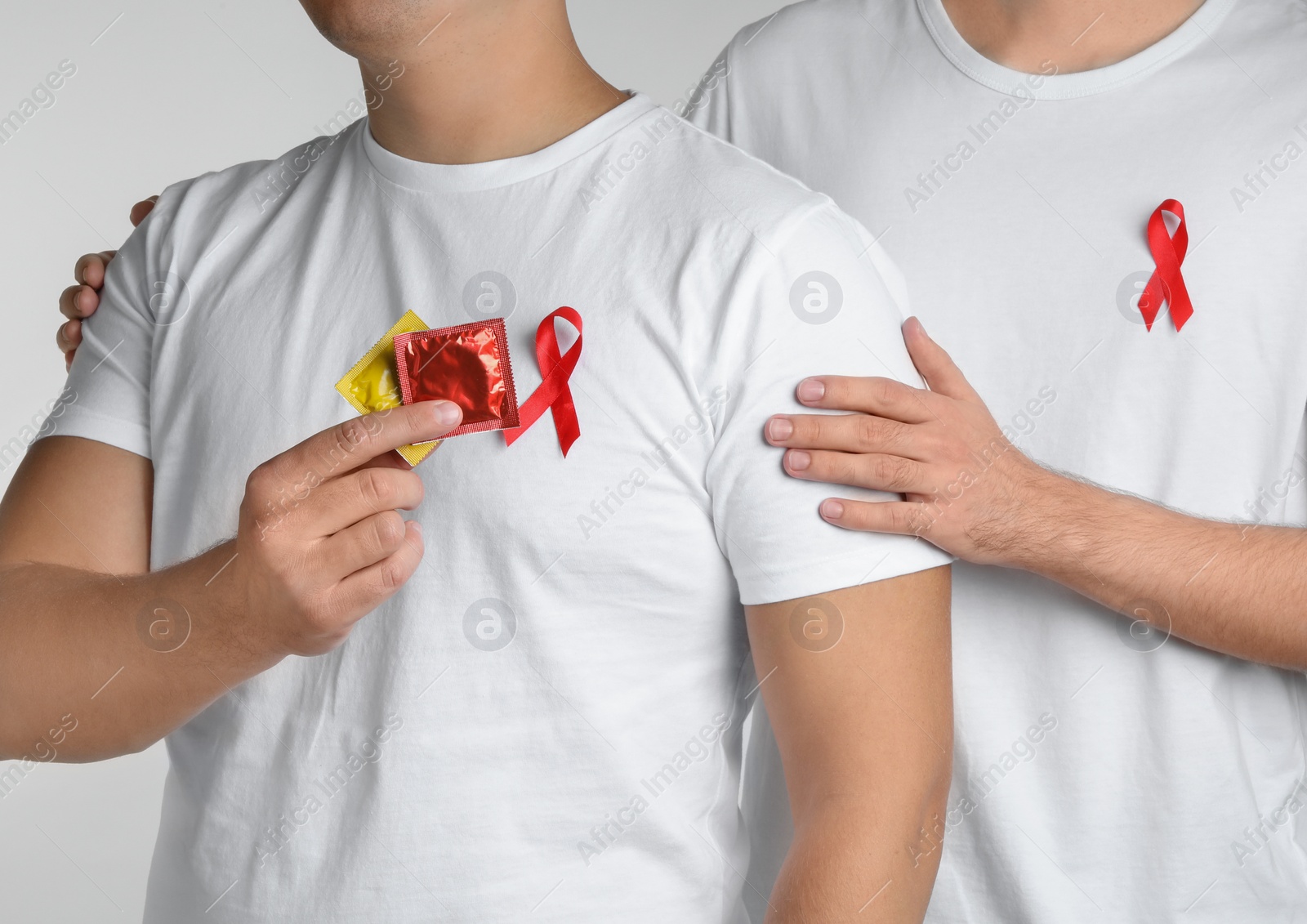 Photo of Men with condoms and AIDS awareness ribbon on white background, closeup