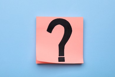 Sticky note with question mark on light blue background, top view