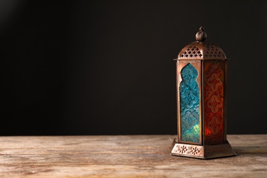 Photo of Muslim lamp with candle on wooden table. Fanous as Ramadan symbol