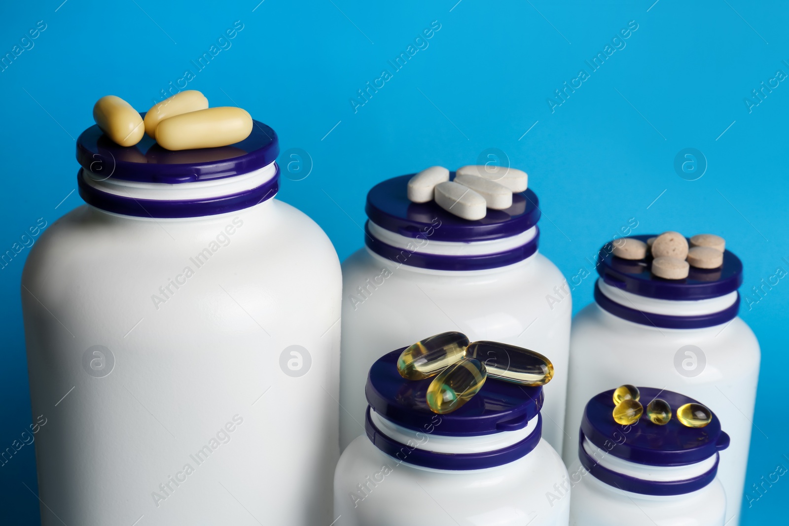 Photo of White medical bottles and different pills on light blue background, closeup