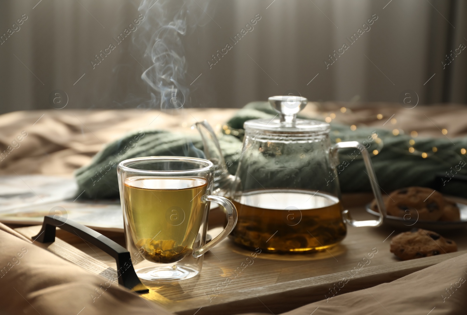 Photo of Wooden tray with freshly brewed tea and cookies on bed in room. Cozy home atmosphere