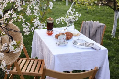 Stylish table setting with beautiful spring flowers, tea and croissants in garden