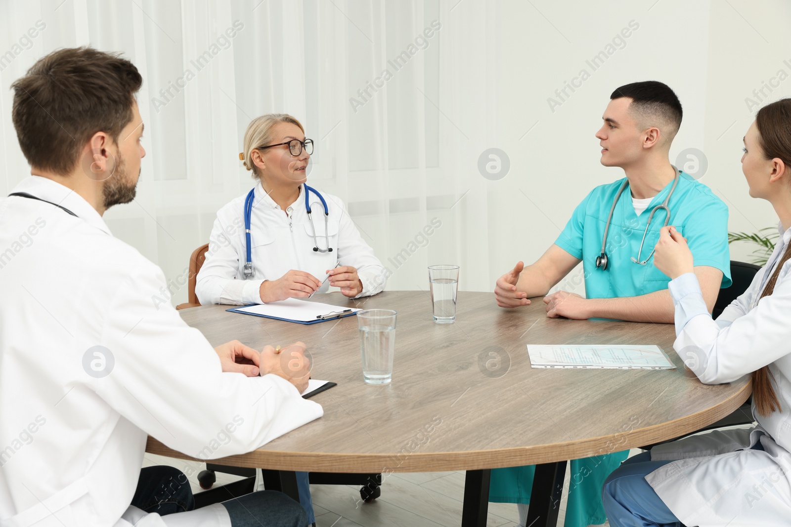 Photo of Medical conference. Team of doctors having discussion at wooden table in clinic