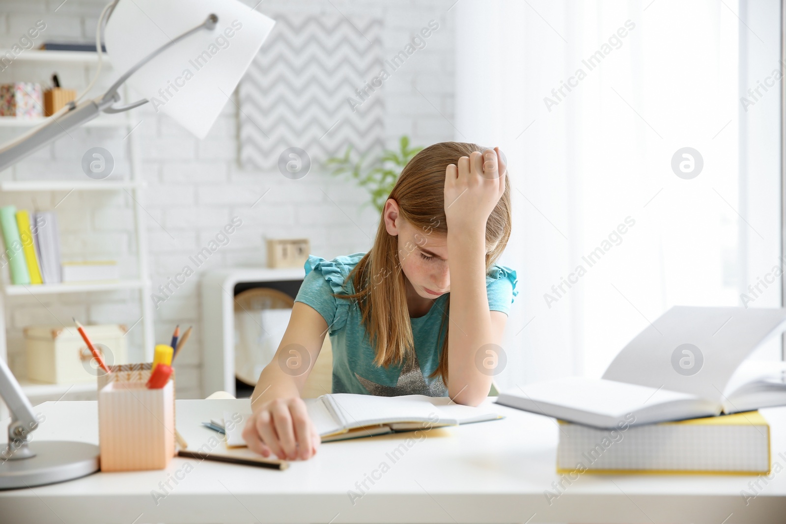 Photo of Teenage girl suffering from headache while doing homework at table indoors