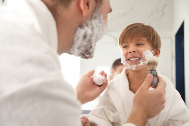 Photo of Dad applying shaving foam onto son's face in bathroom