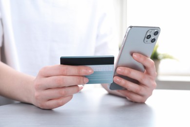 Photo of Online payment. Woman with smartphone and credit card at white table, closeup