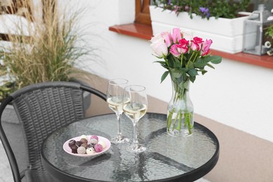 Photo of Vase with roses, glasseswine and candies on glass table near house on outdoor terrace