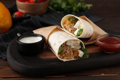 Photo of Delicious tortilla wraps with tuna, vegetables and sauces on wooden table