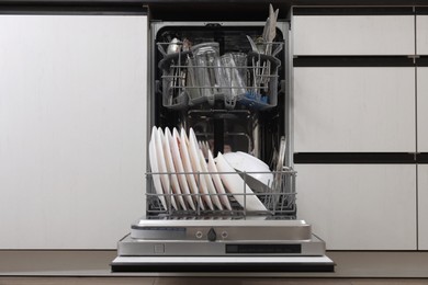 Photo of Open modern dishwasher with dirty tableware in kitchen