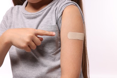 Photo of Girl pointing at sticking plaster after vaccination on her arm against white background, closeup