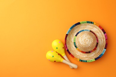 Mexican sombrero hat and maracas on orange background, flat lay. Space for text