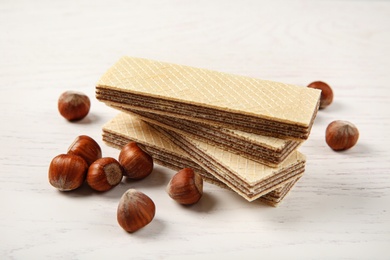 Photo of Delicious wafers with hazelnuts on white wooden background