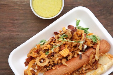 Fresh delicious hot dog with sauce on wooden table, flat lay