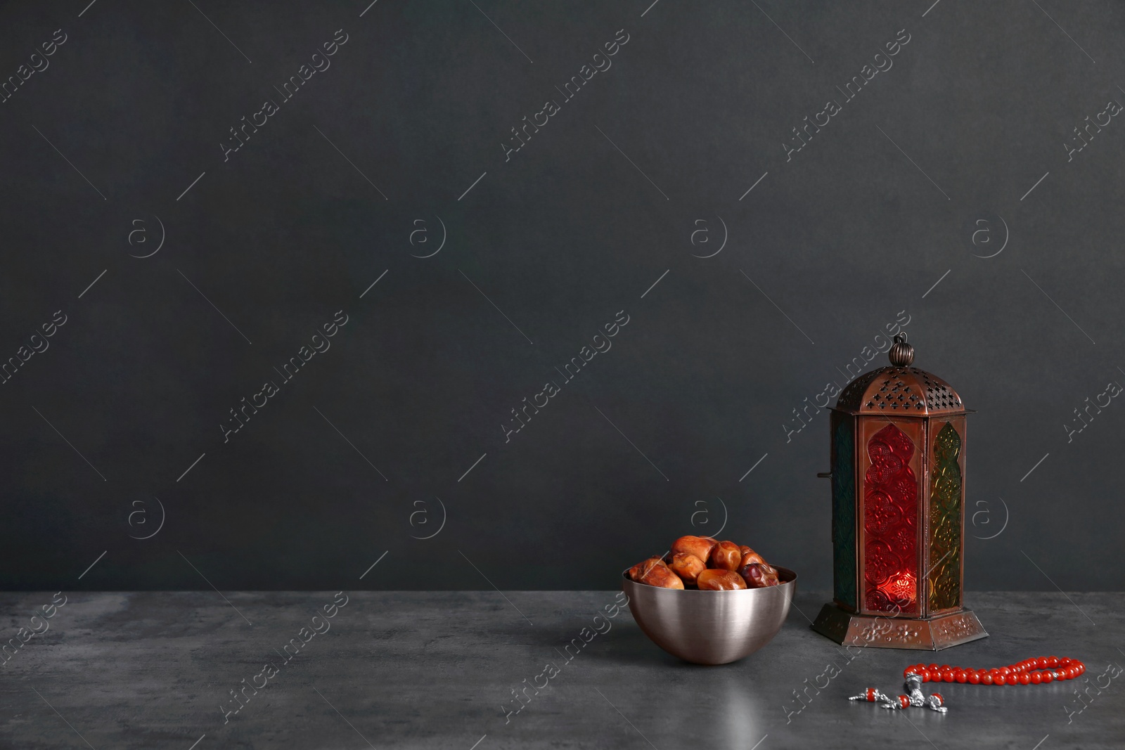 Photo of Muslim lantern Fanous, dried dates and prayer beads on table against dark background. Space for text