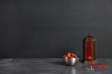 Photo of Muslim lantern Fanous, dried dates and prayer beads on table against dark background. Space for text