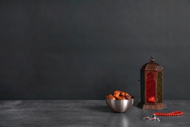 Muslim lantern Fanous, dried dates and prayer beads on table against dark background. Space for text