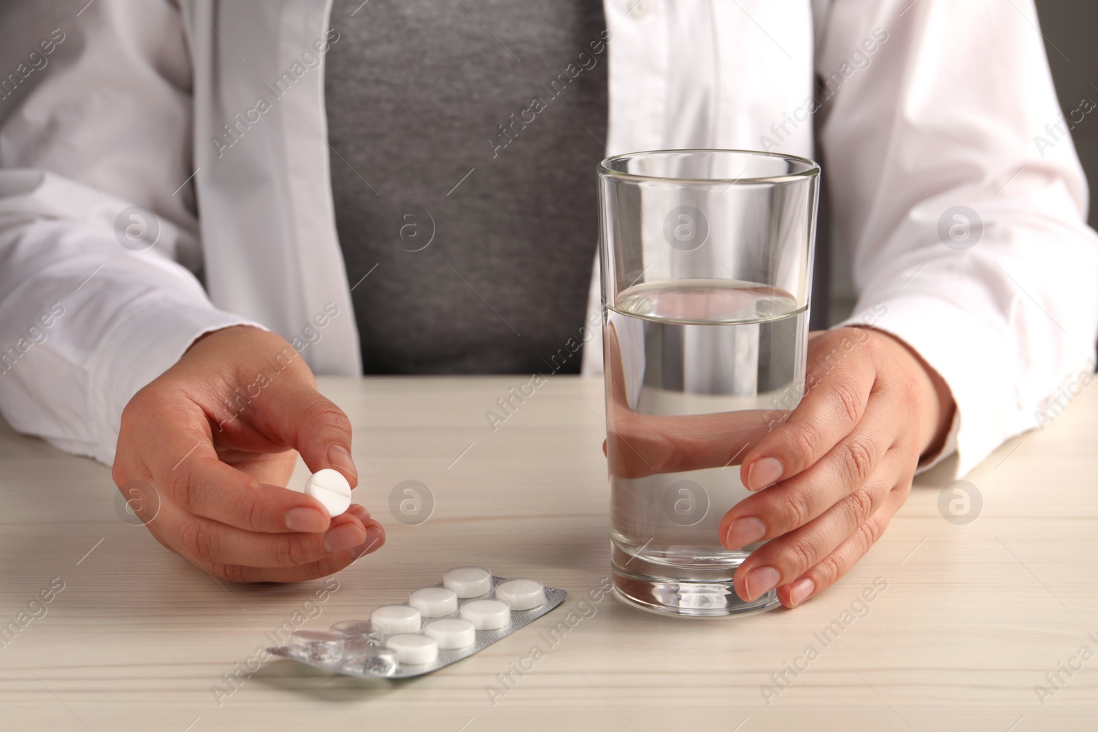 Photo of Woman with pills and glass of water at white wooden table, closeup