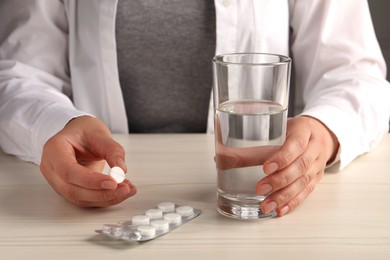 Photo of Woman with pills and glass of water at white wooden table, closeup