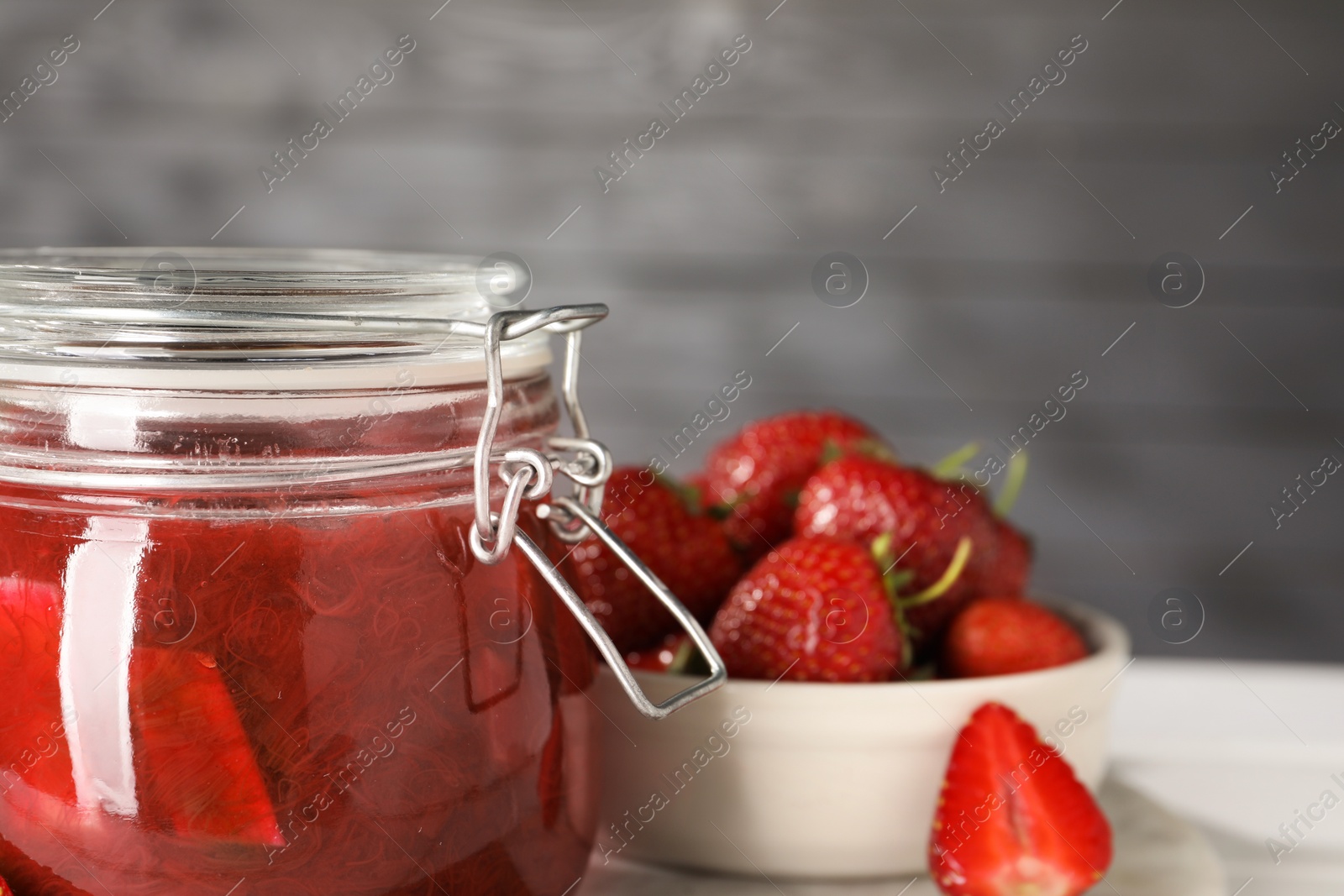 Photo of Jar of tasty rhubarb jam and strawberries on white table, closeup. Space for text