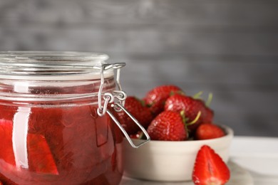 Photo of Jar of tasty rhubarb jam and strawberries on white table, closeup. Space for text