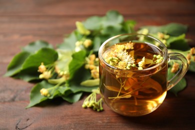 Photo of Cup of tea and linden blossom on wooden table. Space for text