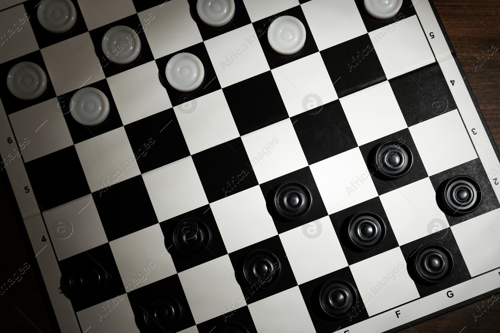 Photo of Checkerboard with game pieces on wooden table, top view