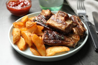 Photo of Delicious grilled ribs with potatoes on table