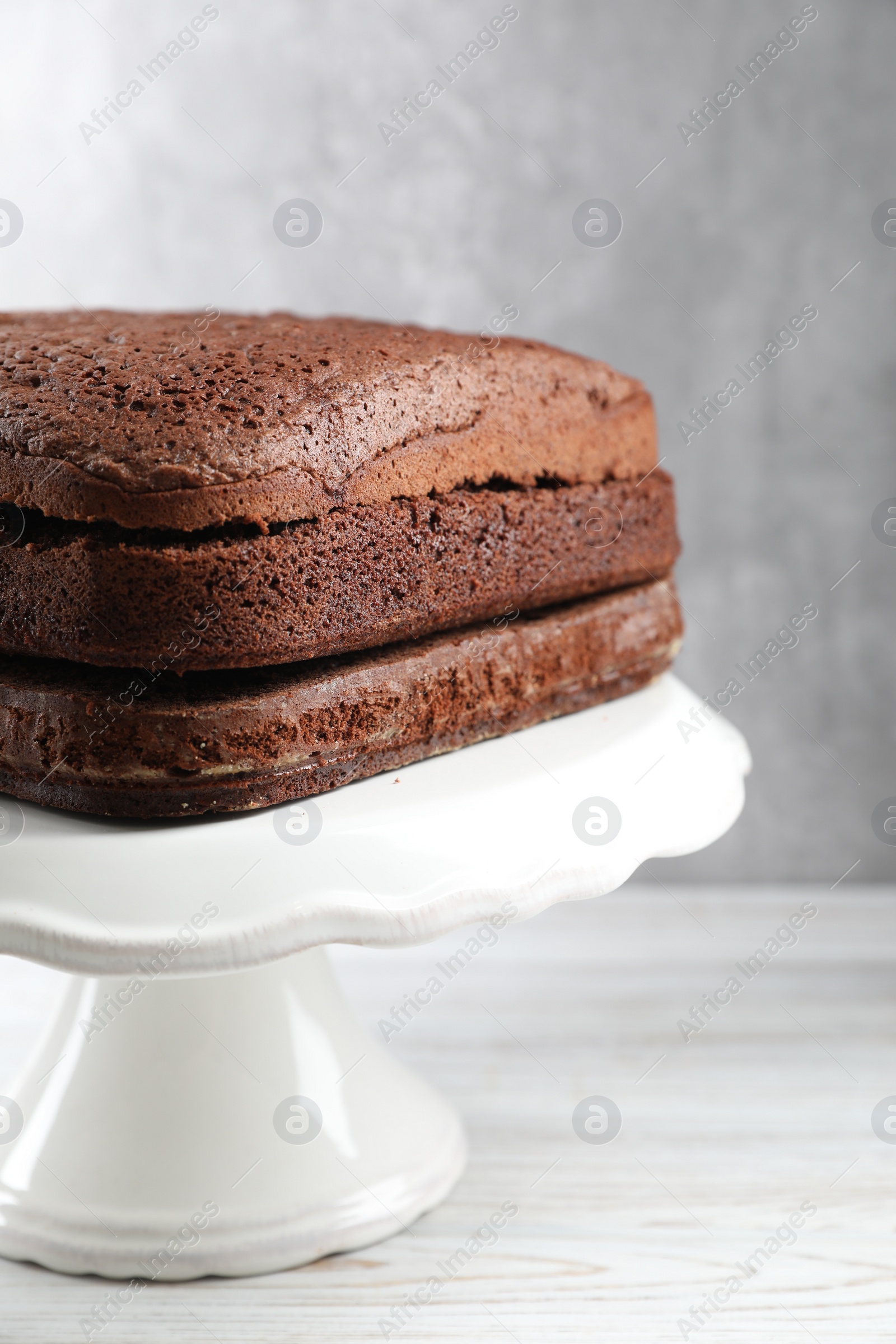 Photo of Stand with layers of homemade chocolate sponge cake on white wooden table
