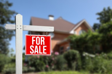 Sale sign near beautiful house outdoors. Red signboard with words