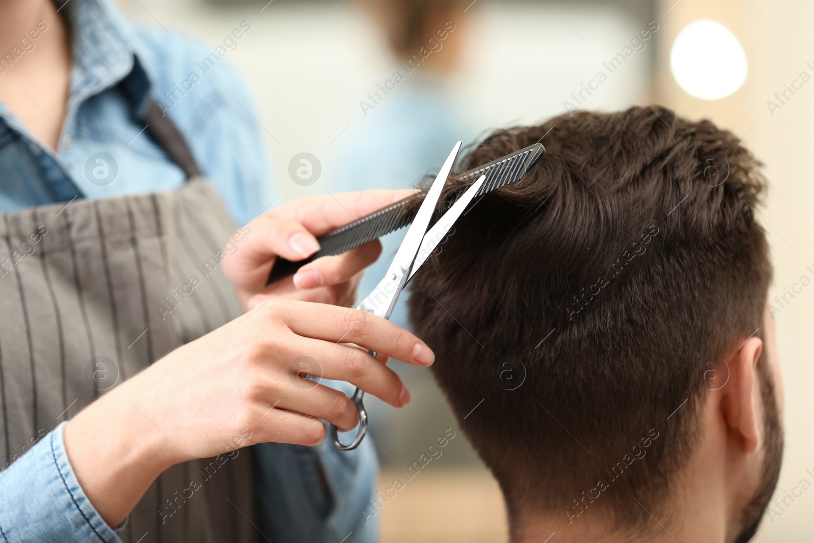 Photo of Barber making stylish haircut with professional scissors in beauty salon, closeup