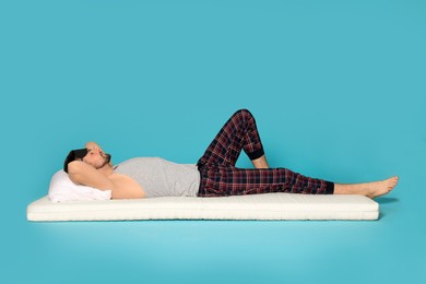 Photo of Man in sleeping mask resting on soft mattress against light blue background