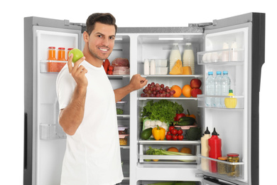 Man with apple near open refrigerator on white background
