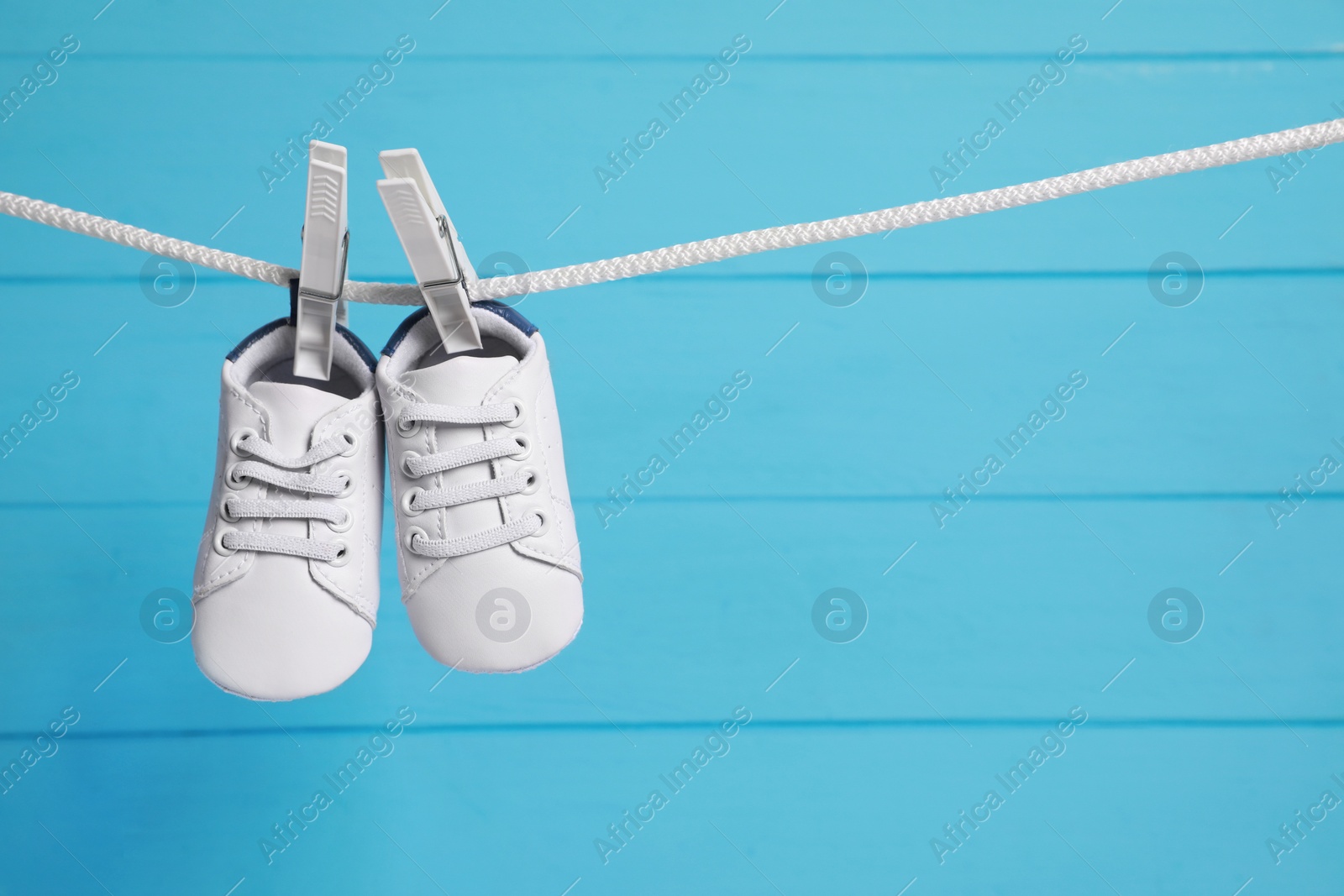 Photo of White baby shoes drying on washing line against light blue wooden wall. Space for text
