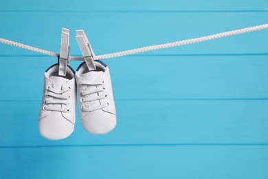 White baby shoes drying on washing line against light blue wooden wall. Space for text