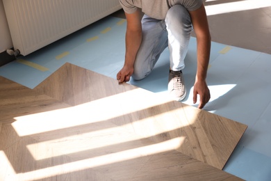 Worker installing laminated wooden floor indoors, closeup