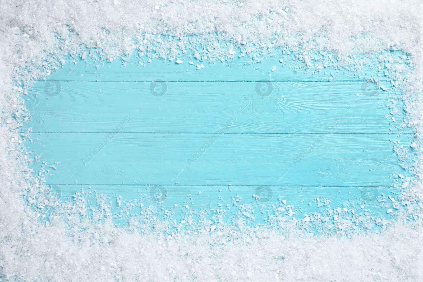 Photo of Frame of white snow on light blue wooden background, top view with space for text. Christmas season